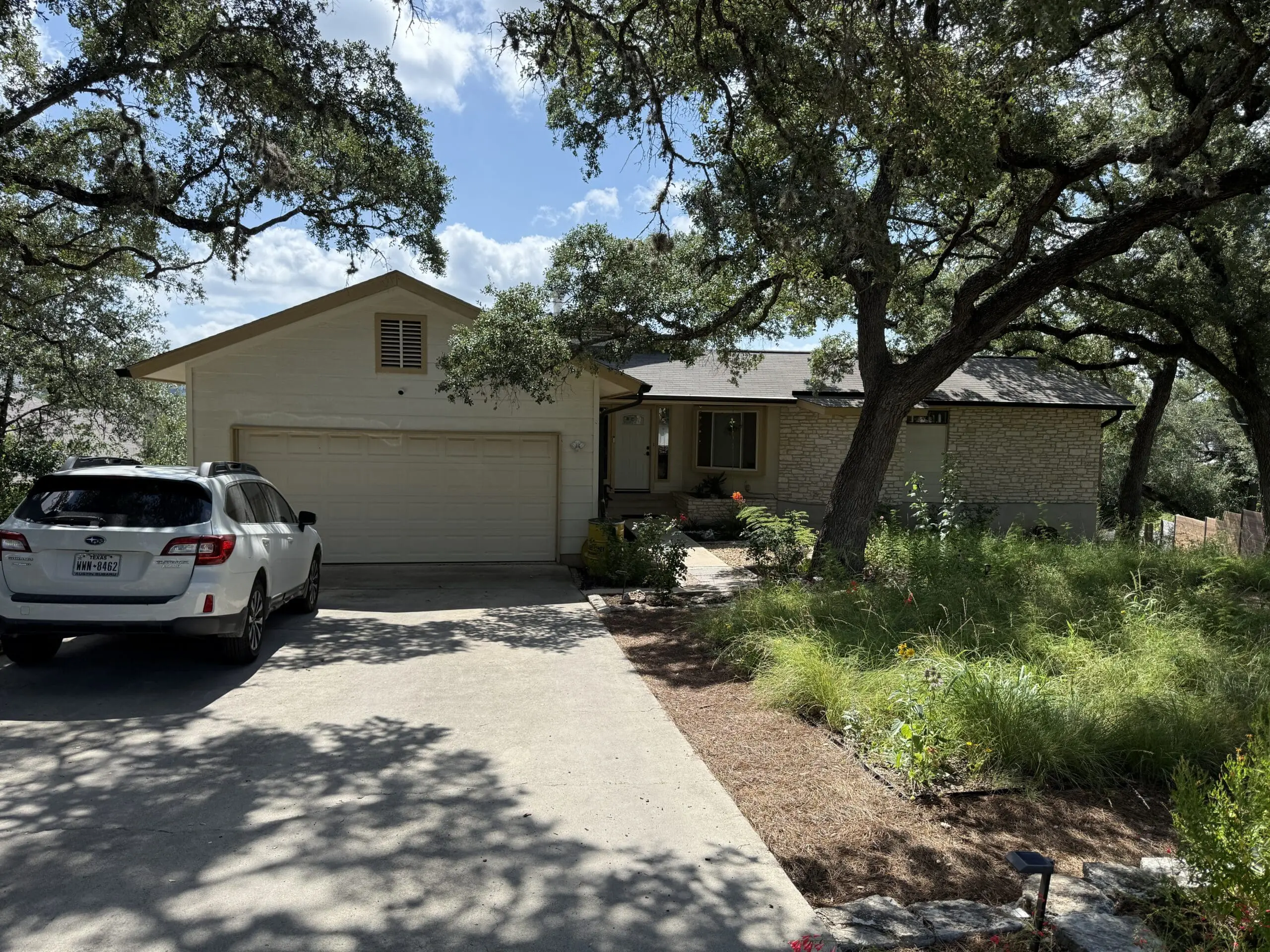 Exterior house painting on an Austin, TX home with cream siding, tan trim, a painted garage door and front entry, and a limestone facade under mature live oaks