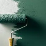 Paint roller applying green interior paint to a wall, showing paint finish mid-application.