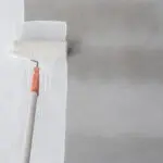 Paint roller applying white paint to an interior wall showing the professional painting process mid-application.