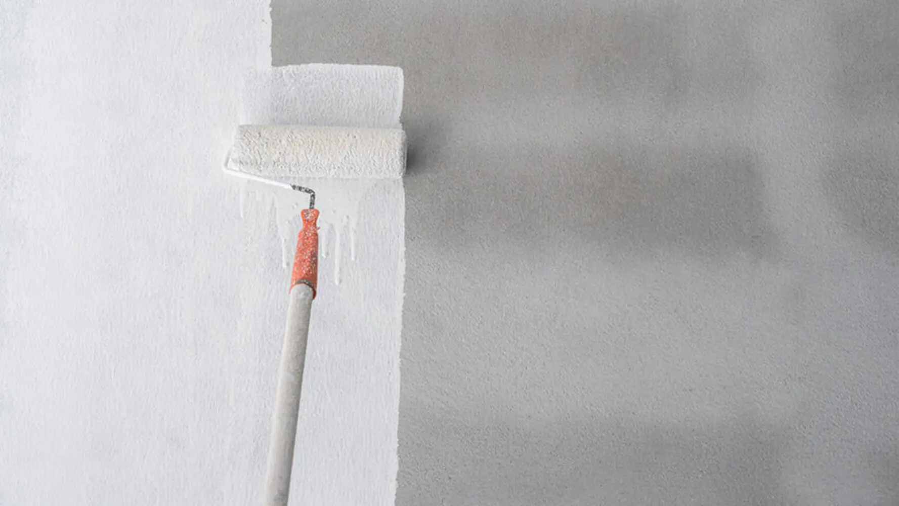 Paint roller applying white paint to an interior wall showing the professional painting process mid-application.