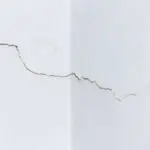 Cracks spreading across an interior drywall wall corner showing signs of drywall damage that needs professional repair.