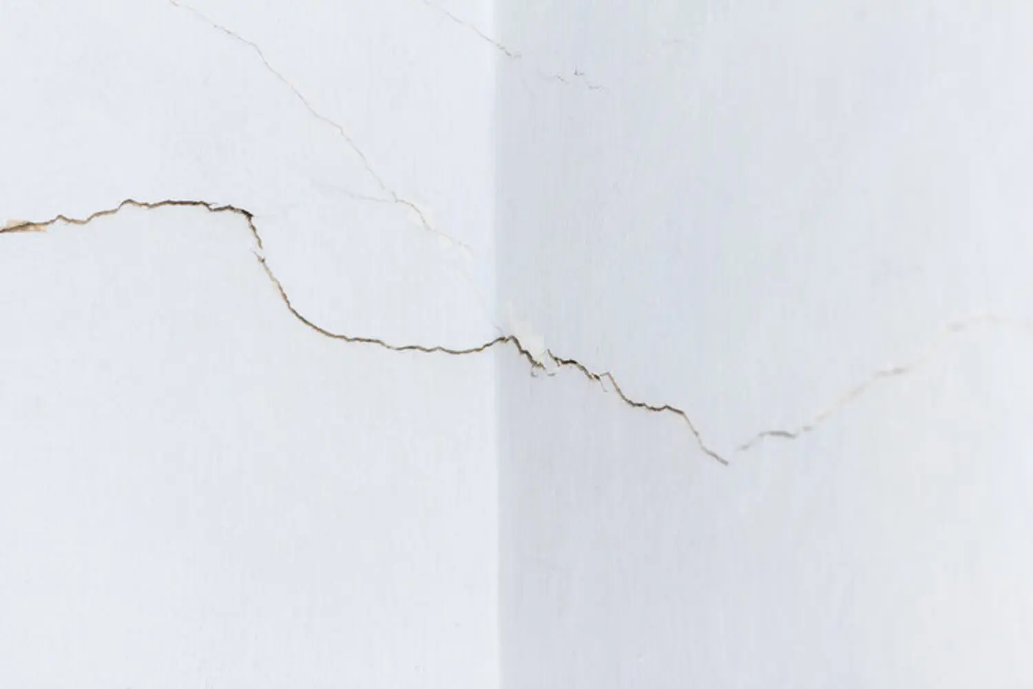 Cracks spreading across an interior drywall wall corner showing signs of drywall damage that needs professional repair.