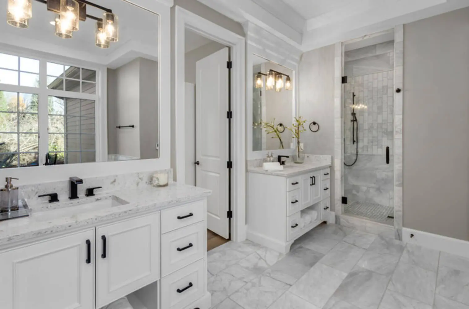 Remodeled primary bathroom with white dual vanities, marble tile flooring, and a glass walk-in shower showing finished bathroom renovation results.
