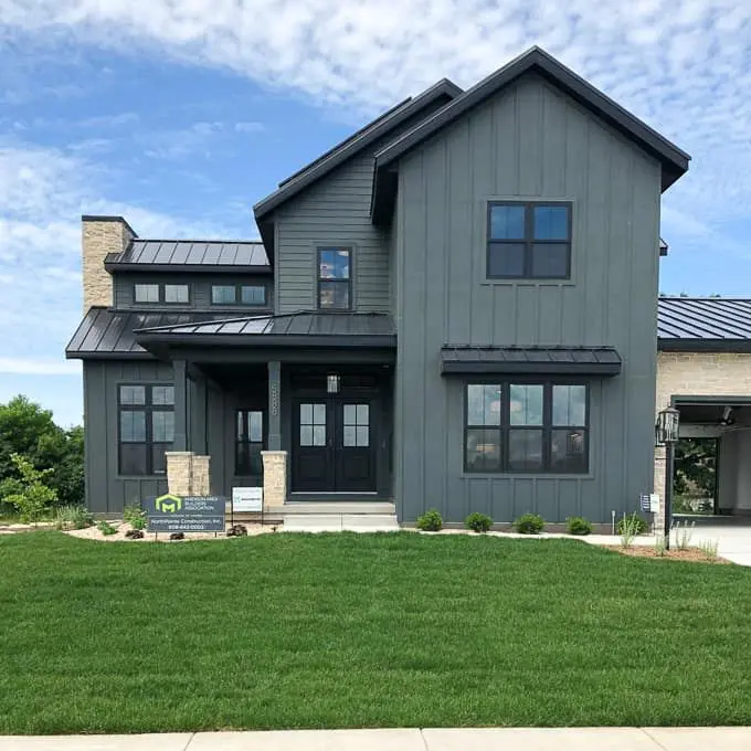 Exterior house painting on a modern farmhouse in Austin, TX with dark green-gray board and batten and lap siding, black window frames and doors, stone accents, and a standing seam metal roof