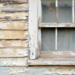 Peeling and cracking exterior paint on wood siding near a window frame showing paint failure.