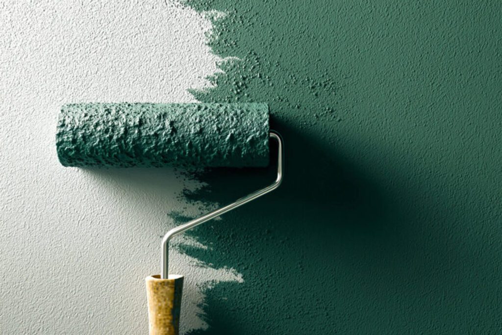 Paint roller applying green interior paint to a wall, showing paint finish mid-application.