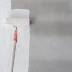Paint roller applying white paint to an interior wall showing the professional painting process mid-application.