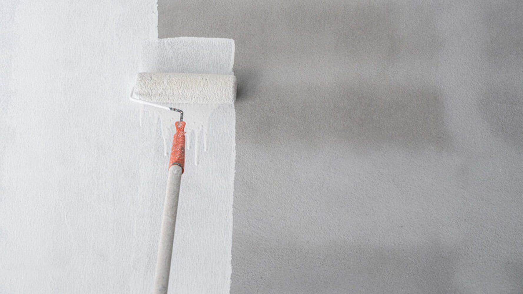 Paint roller applying white paint to an interior wall showing the professional painting process mid-application.