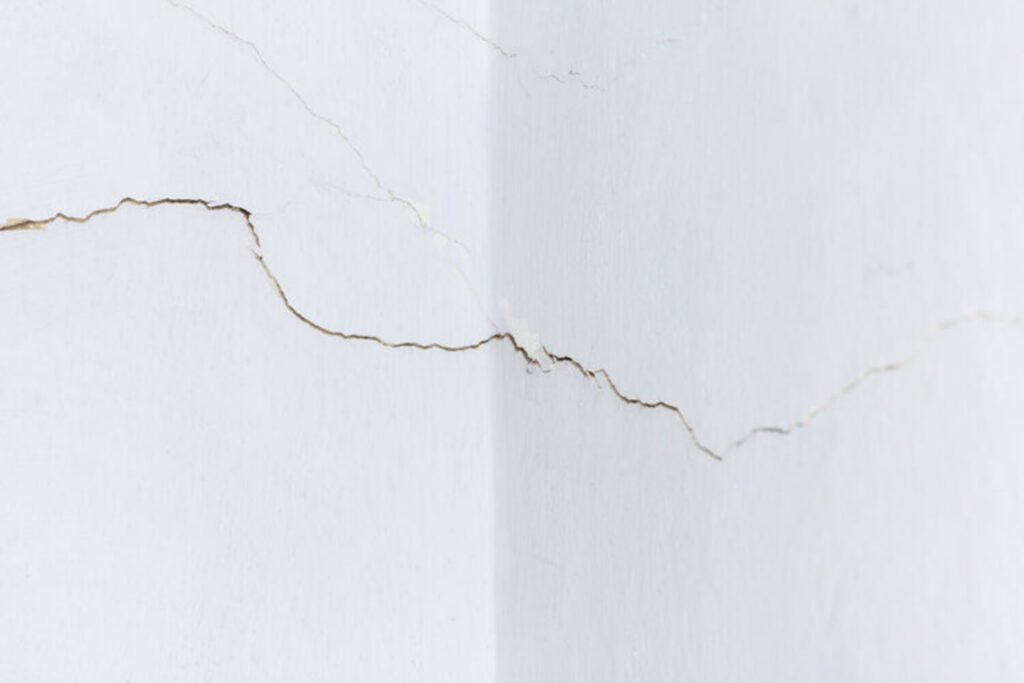 Cracks spreading across an interior drywall wall corner showing signs of drywall damage that needs professional repair.