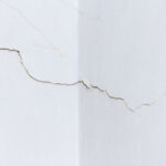 Cracks spreading across an interior drywall wall corner showing signs of drywall damage that needs professional repair.