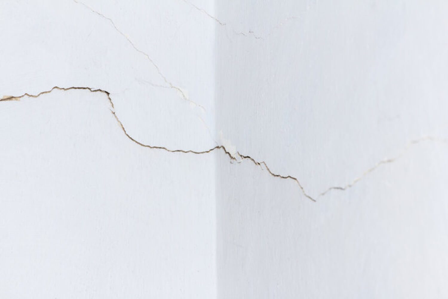 Cracks spreading across an interior drywall wall corner showing signs of drywall damage that needs professional repair.