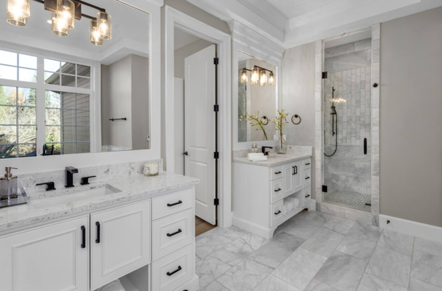 Remodeled primary bathroom with white dual vanities, marble tile flooring, and a glass walk-in shower showing finished bathroom renovation results.