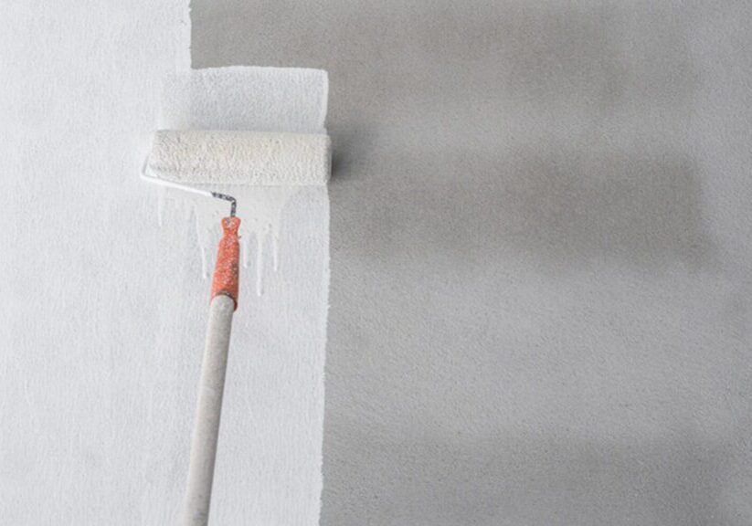 Paint roller applying white paint to an interior wall showing the professional painting process mid-application.