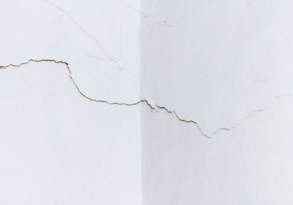 Cracks spreading across an interior drywall wall corner showing signs of drywall damage that needs professional repair.