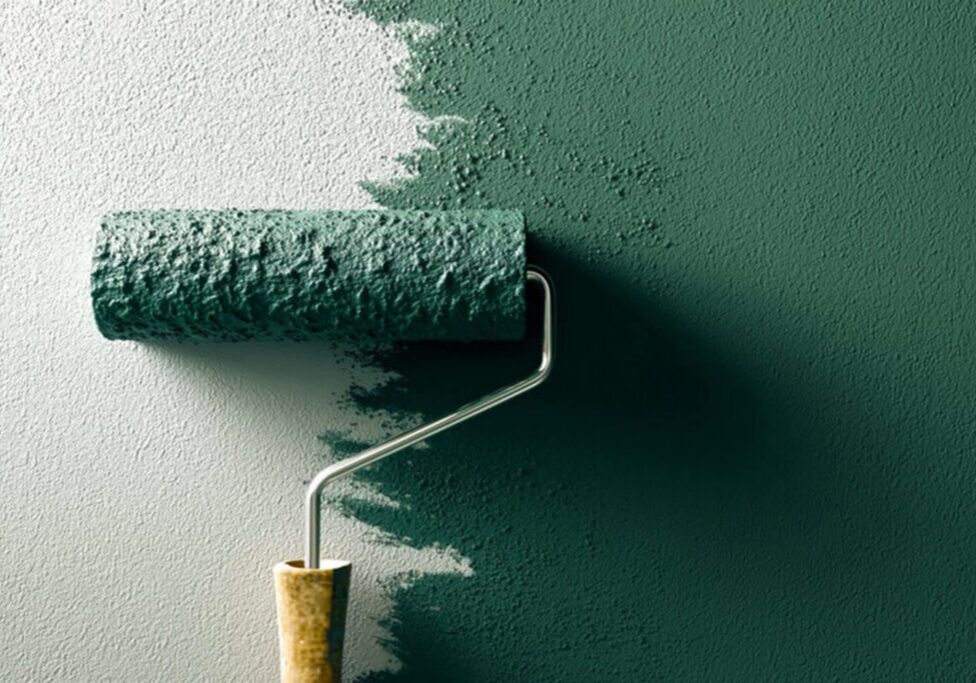 Paint roller applying green interior paint to a wall, showing paint finish mid-application.
