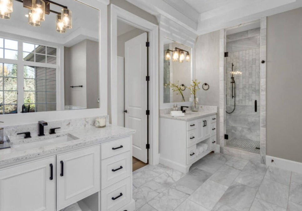 Remodeled primary bathroom with white dual vanities, marble tile flooring, and a glass walk-in shower showing finished bathroom renovation results.